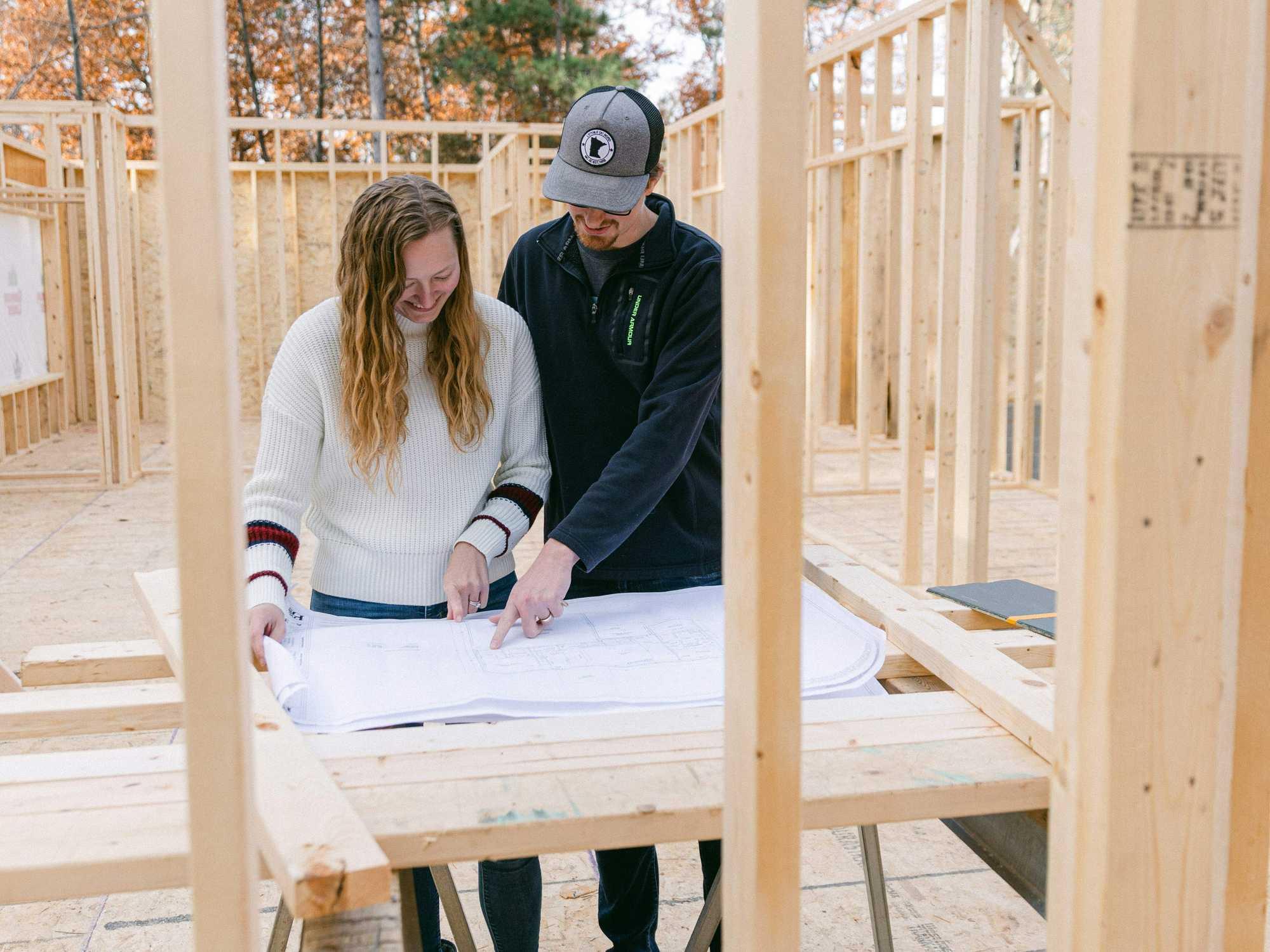A man and a woman standing inside of a house under construction.